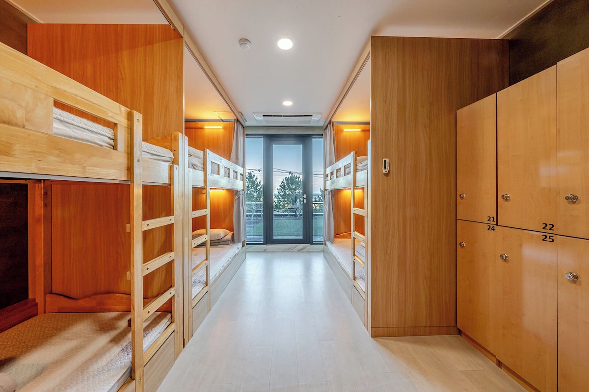 Un pasillo con literas y taquillas de madera, que conduce a una puerta con vistas al exterior.