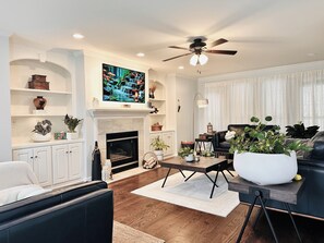 A living room with a fireplace, a television mounted above it, and a ceiling fan. - 2027 Masters Rental House with Private Saltwater Pool & Jacuzzi bathtub (Evans)