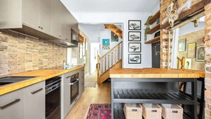A modern kitchen with a brick backsplash, wooden countertop, and a black shelving unit with baskets. - Darlinghurst Sky Deck Home | City at Your Feet (Darlinghurst)