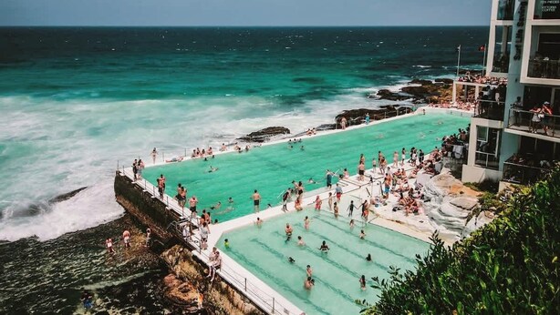 A large outdoor swimming pool with clear turquoise water, surrounded by rocky cliffs and overlooking the ocean. - Darlinghurst Sky Deck Home | City at Your Feet (Darlinghurst)