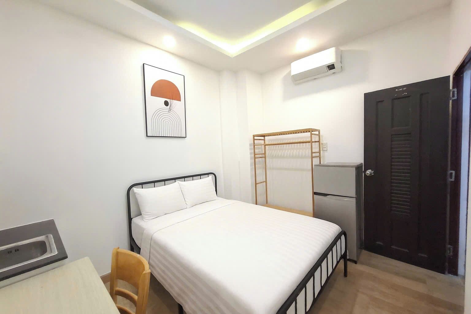 A single bed with a headboard, a desk with a chair, a wall-mounted air conditioner, and a door.
