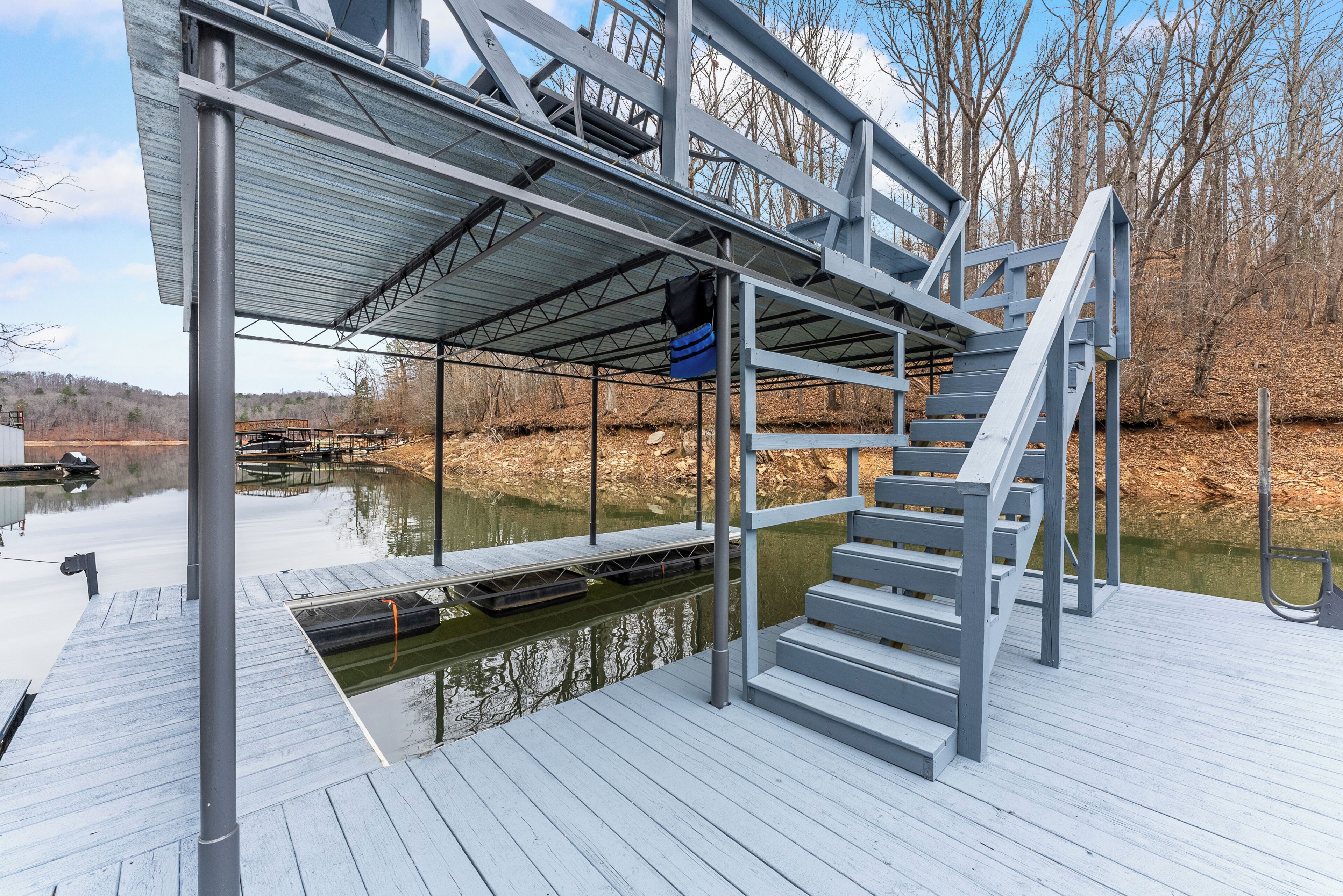 A dock with a metal staircase leading to a covered area, a calm body of water, and trees in the background.