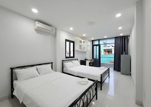 Une chambre d’hôtel avec deux lits, une kitchenette et un balcon donnant sur des immeubles.