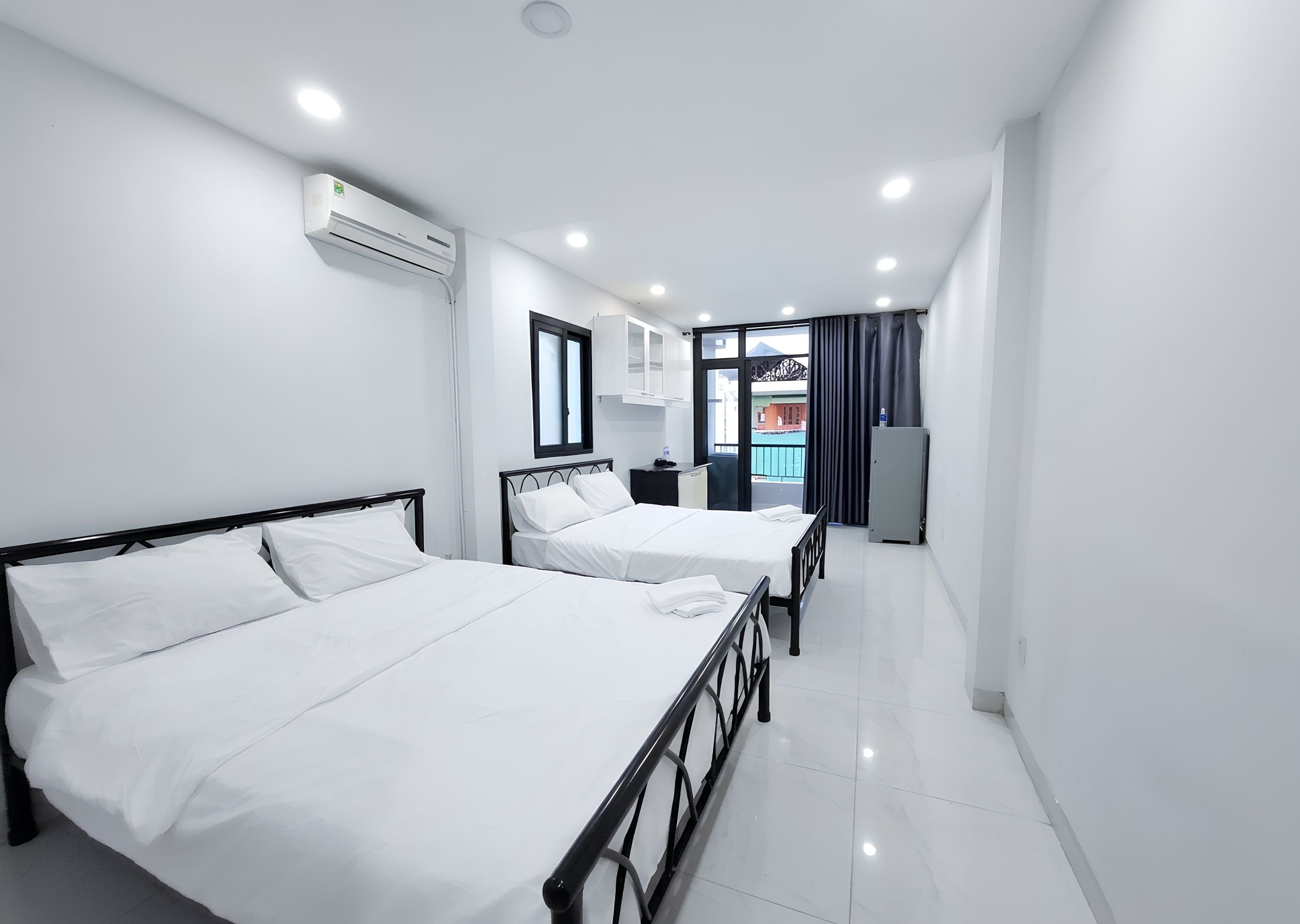 A hotel room with two beds, a window, an air conditioning unit, and a view of the outside.