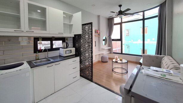Eine moderne Küche mit weißen Schränken, einer Mikrowelle und einem Wasserkocher. Ein Fenster bietet Blick auf Gebäude und es gibt einen Balkon.