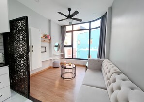 Un salon moderne avec un canapé, une table basse ronde, un ventilateur de plafond et une grande fenêtre avec des rideaux.