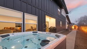 Un jacuzzi se trouve devant une maison, et la porte du garage est ouverte, révélant un salon avec un canapé et une table à manger.