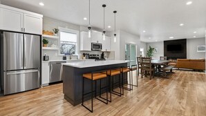 Une cuisine moderne dotée d’appareils électroménagers en acier inoxydable, d’un îlot central avec des tabourets, et d’un coin repas avec une table et des chaises en bois.
