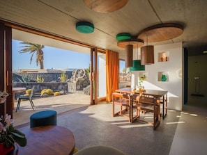 A modern interior with a dining area, a view of the outdoors, and a shower area. - Canaryislandshost I Famara Soul Suite (Urbanización Famara)