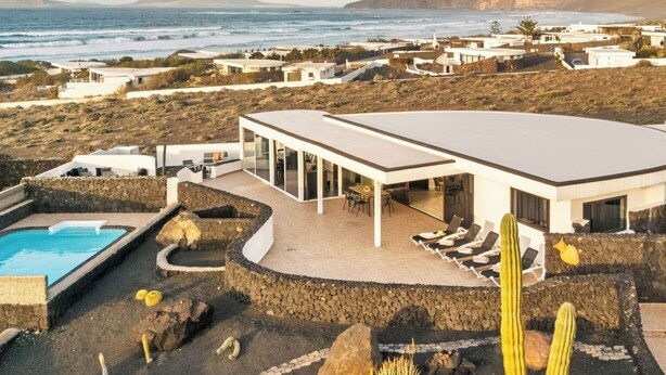 Uma villa moderna com piscina, área de estar externa e vista para o oceano e montanhas.