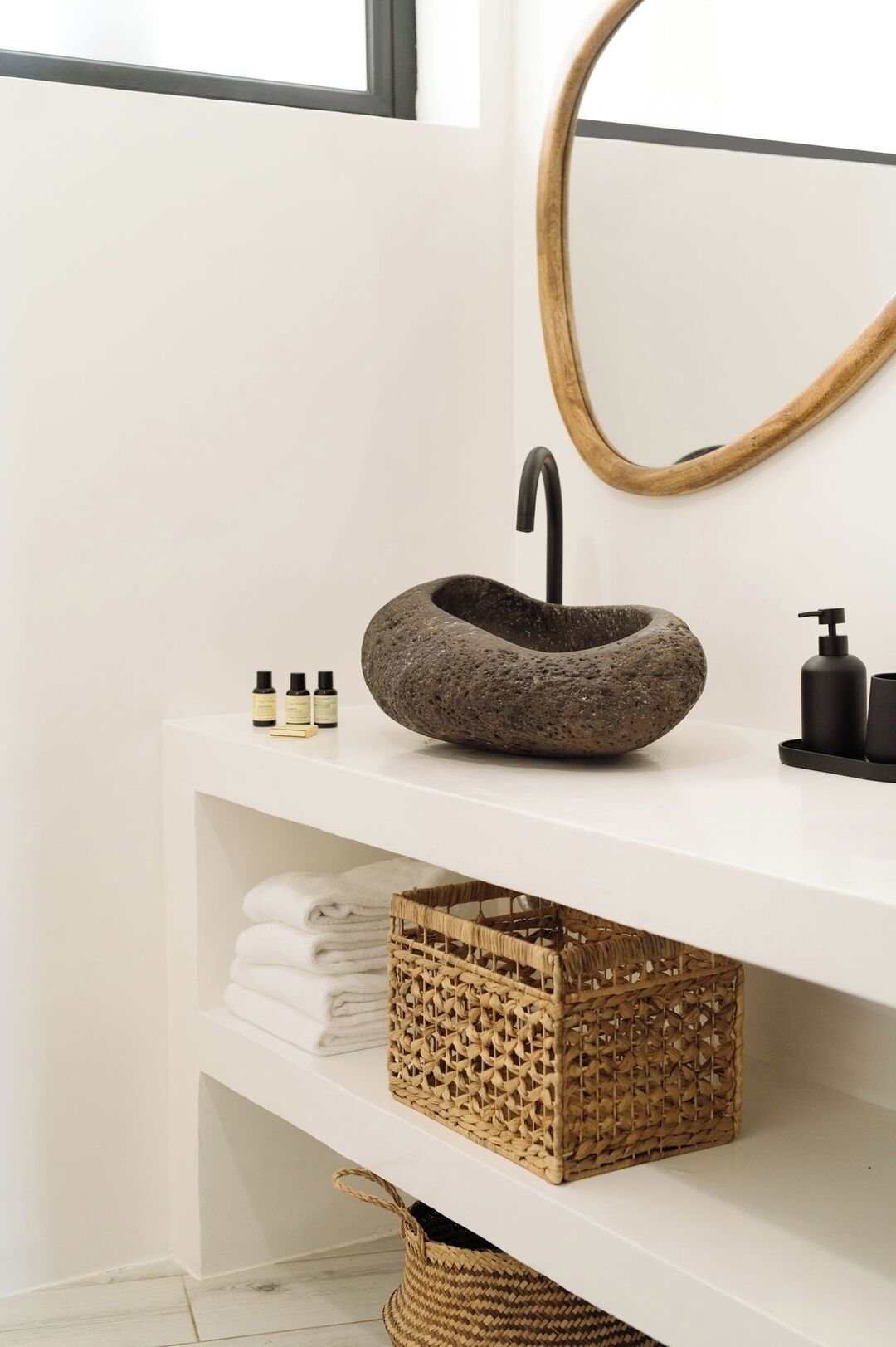 Une salle de bain avec un lavabo en pierre, un miroir et une étagère où sont posées des serviettes et des paniers.