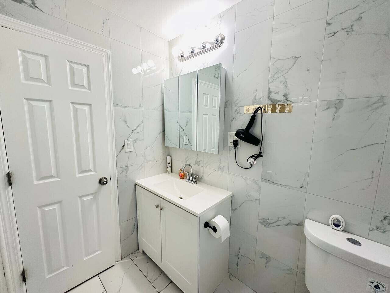 A bathroom with a white sink, a mirror, a toilet, and a hairdryer on the wall.