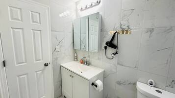 A bathroom with a white sink, a mirror, a toilet, and a hairdryer on the wall.