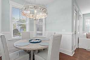 A dining area with a round wooden table, striped chairs, and a decorative chandelier. - Seas the Day! Elegant 4BR 30A Retreat with Golf Cart & Bikes (Santa Rosa Beach)