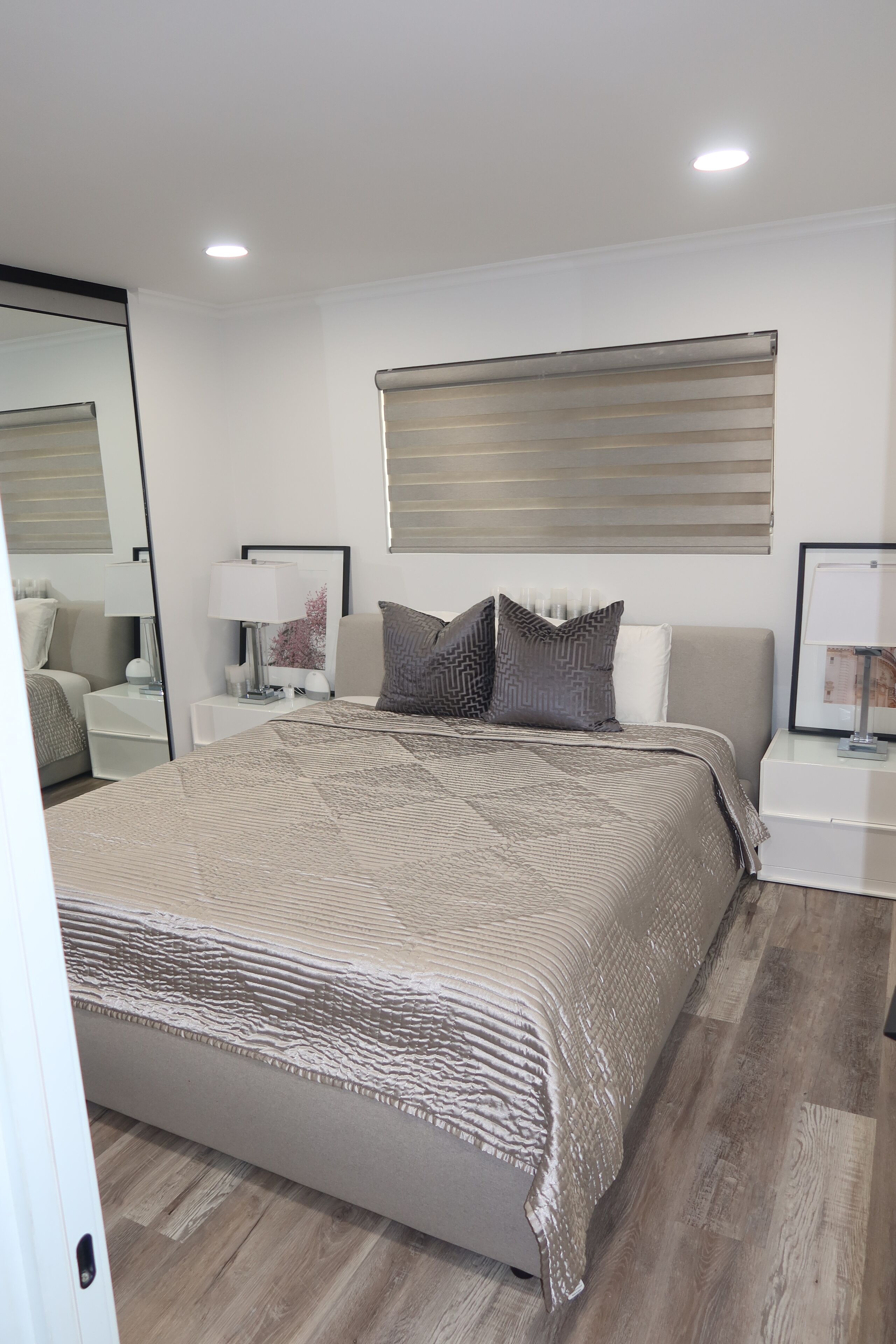 A modern bedroom with a large bed, two bedside tables, a mirror, and a ceiling light.