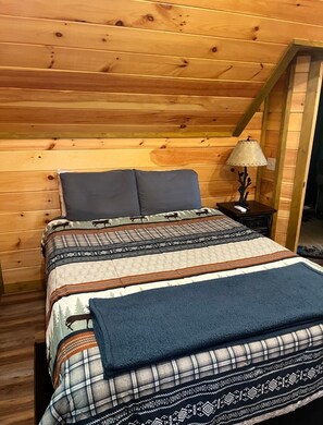 Ein Zimmer mit Holzwänden, einem Bett, einem Nachttisch und einer Lampe.