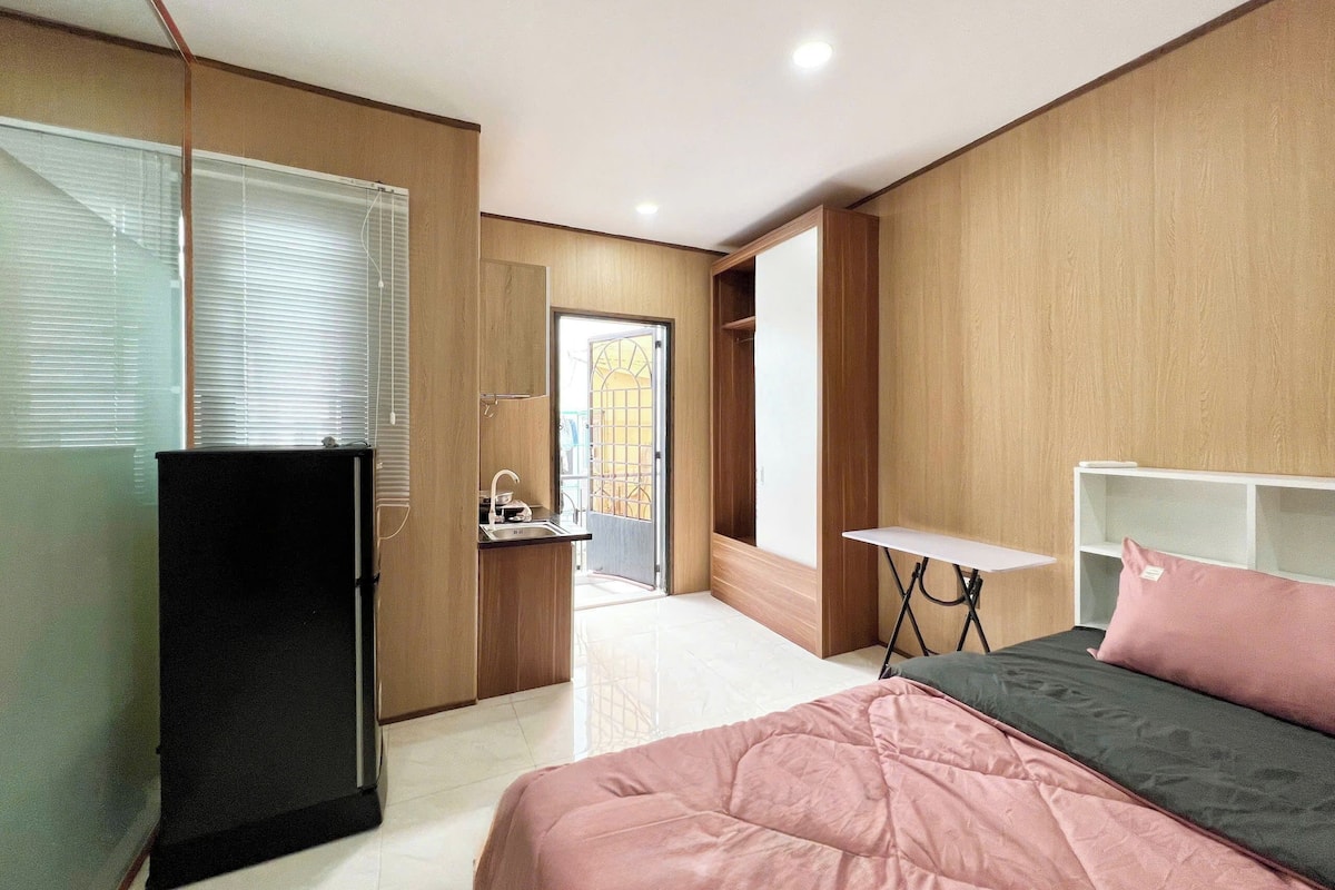 A bedroom with a bed, a desk, a refrigerator, and a bathroom visible through an open door.