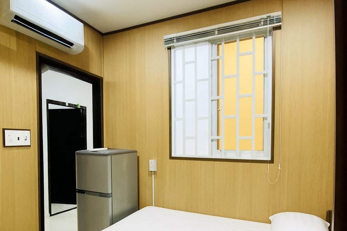 A bedroom with a bed, a wardrobe, an air conditioning unit, and a window with blinds.