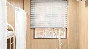 Ein Zimmer mit Etagenbett, Tisch, Fenster mit Jalousien und Klimaanlage.