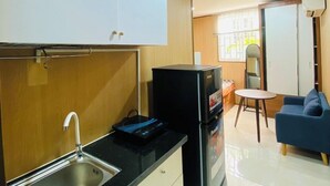 Eine kompakte Küche mit Spüle, einem schwarzen Kühlschrank und einer kleinen Essecke mit einem blauen Sofa.