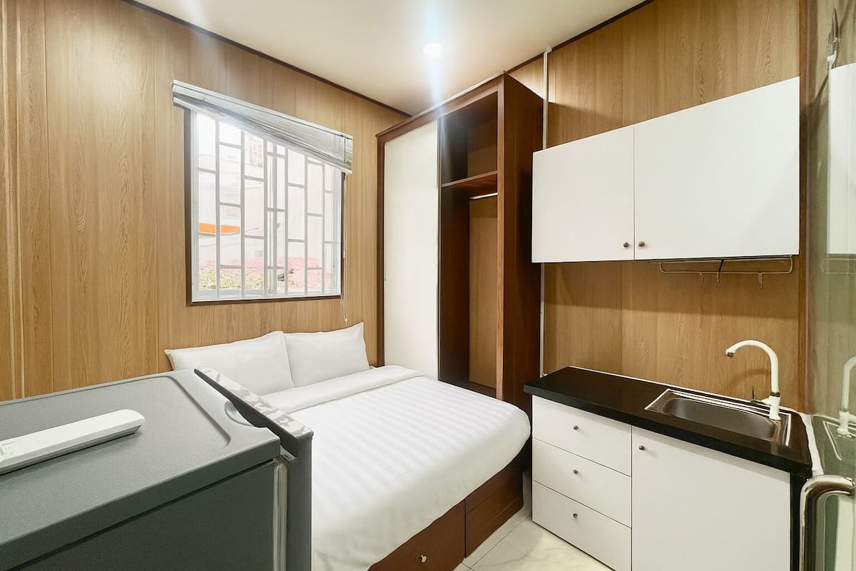 A bedroom with a bed, a desk, a wardrobe, and a bathroom with a sink.