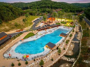 Een resort met een groot zwembad, terras en uitzicht op het omliggende bos.