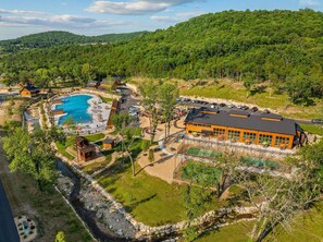 Luchtbeeld van een resort met een zwembad, gastcabines en een tennisbaan.