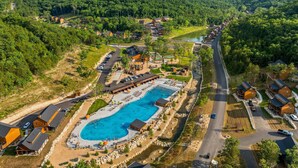 An aerial view of a resort with a swimming pool, guest cabins, and a river. - 2BR Tall Timbers Cabin | Hot Tub | Sleeps 8 | Free Tickets (Hollister)