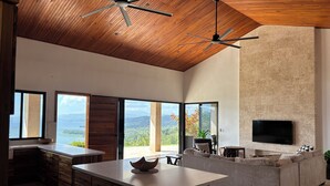 A modern kitchen with a central island, large windows, and a stone wall. - Panoramic Lake Arenal Sunset View Villa with AC (Nuevo Arenal)