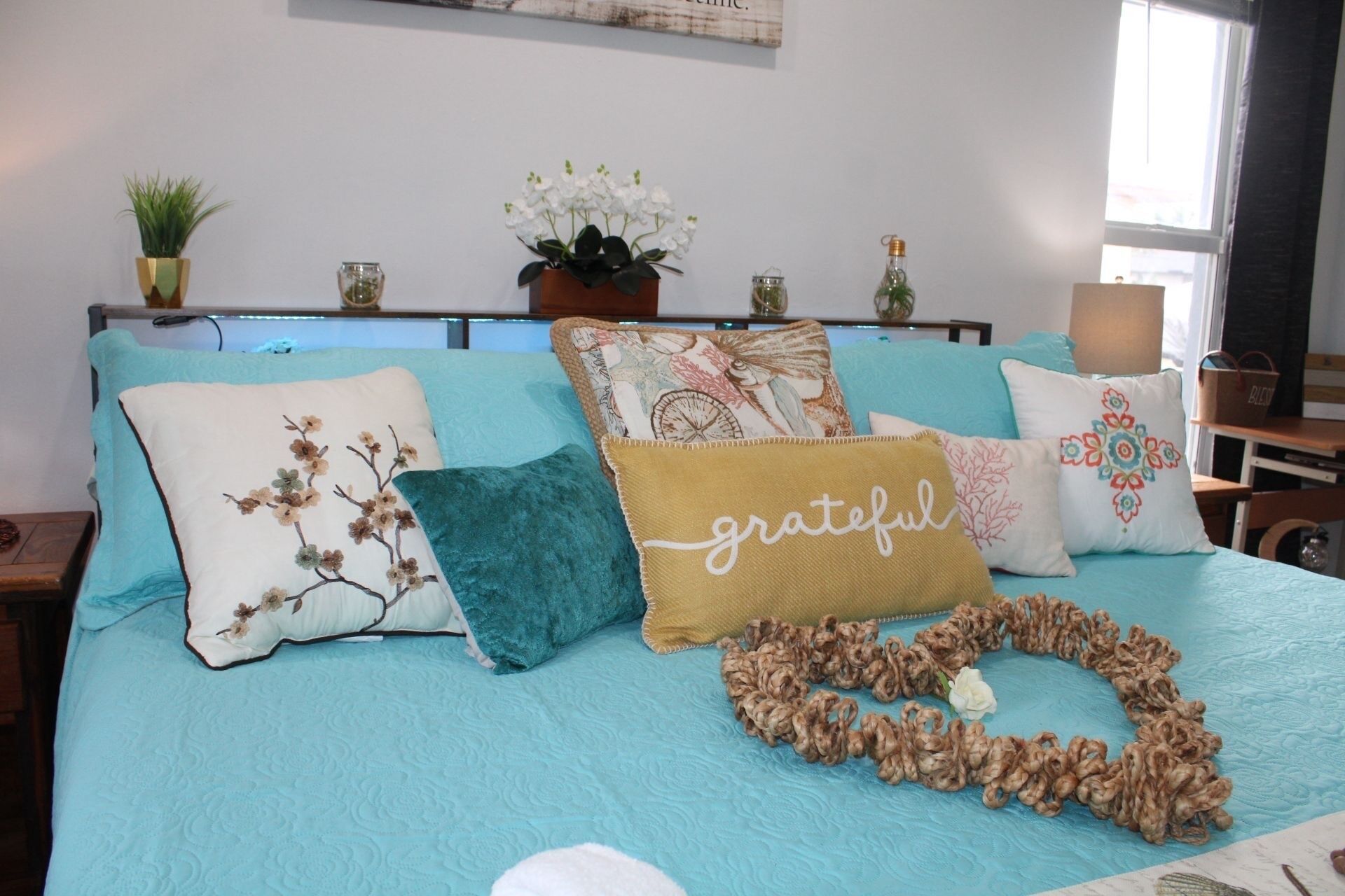 Een bed met meerdere kussens, een decoratieve guirlande en een aan de muur bevestigde plant.