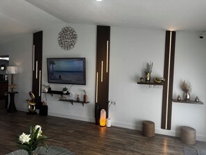 Ein modernes Wohnzimmer mit Flachbildfernseher an der Wand, Holzböden und dekorativen Regalen mit Pflanzen und Vasen.
