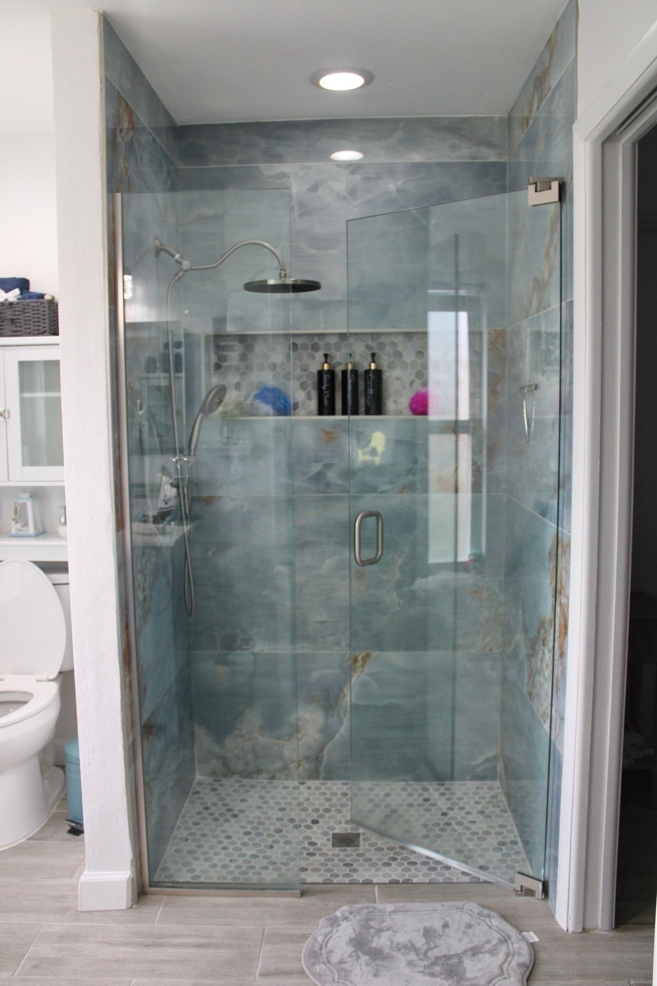 Une douche fermée par des parois en verre, dotée d’un pommeau de douche à effet pluie, d’un pommeau de douche à main et d’une porte en verre avec une poignée argentée.