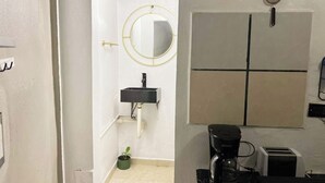 Une salle de bain avec un lavabo blanc, un miroir, une petite plante en pot et une machine à café.