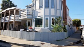 A two-story house with a white exterior, a balcony on the second floor, and a small front yard with a white picket fence. - Walk to the Beach! Stylish Newport Retreat Near Dining, Shops & the Boardwalk (Newport Beach)