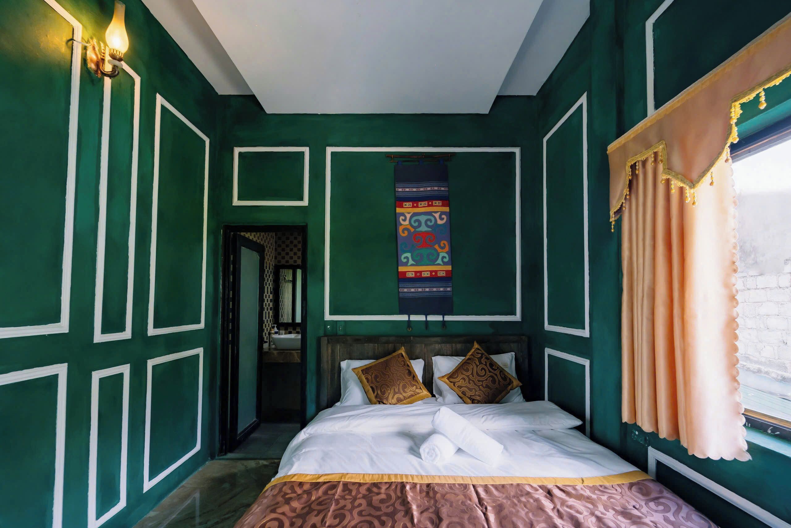 Un dormitorio con cama, una ventana con cortinas, un aplique de pared y un tapiz decorativo.