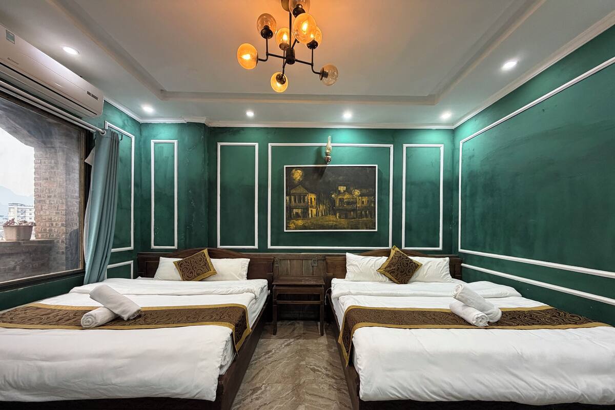 Une chambre d’hôtel avec deux lits, un lustre, un tableau et une fenêtre avec des rideaux.