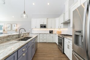 A modern kitchen with white cabinets, a stainless steel refrigerator, a built-in oven, and a marble countertop. - Wake and Lake - Prime Location, Stunning Views! (Littleton)