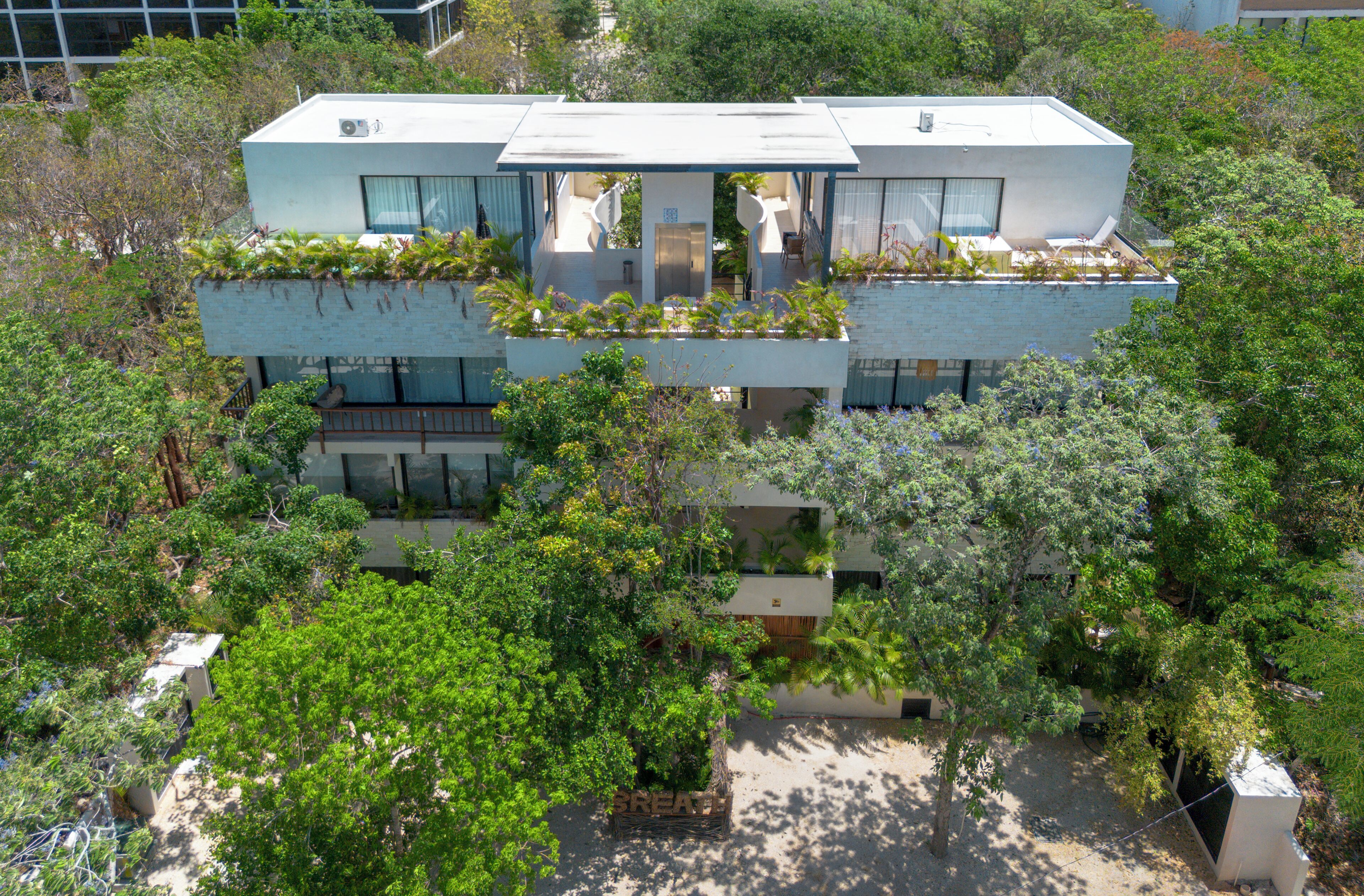 A modern two-story building with a flat roof, large windows, and a balcony with plants.