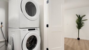 Un espace buanderie comprenant deux machines à laver superposées, une porte et un pot de fleurs.
