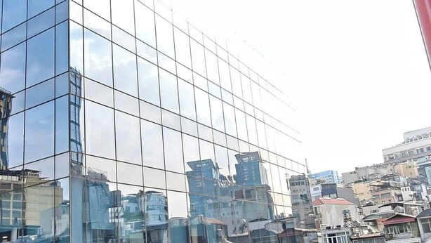 Un bâtiment moderne en verre, doté d’une façade réfléchissante, entouré d’autres immeubles et de verdure.