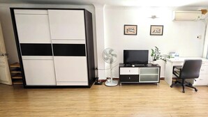 Une chambre équipée d’une armoire, d’un bureau avec une chaise, d’un ventilateur et d’une télévision.