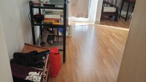 Une pièce avec un plancher en bois, un téléviseur fixé au mur, une bibliothèque et une chaise.