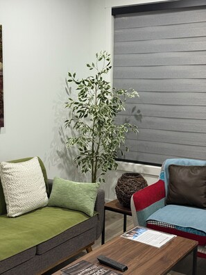 A living room with a sofa, a coffee table, a plant, and a window with blinds.
