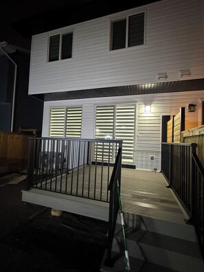 A two-story building with a garage door, a small porch with a railing, and a staircase leading to the entrance. - Slice of Heaven - Near Spruce Meadows - 2 Car Garage Central AC avail -Sleeps 8  (Calgary)