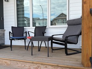 A porch with three chairs, a small table, and a wooden deck.