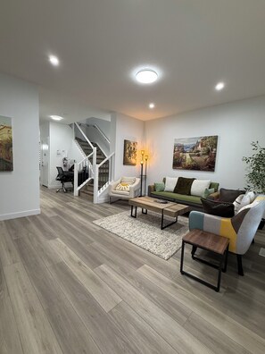 A modern living room with a staircase, a green sofa, a wooden coffee table, and a painting on the wall. - Slice of Heaven - Near Spruce Meadows - 2 Car Garage Central AC avail -Sleeps 8  (Calgary)
