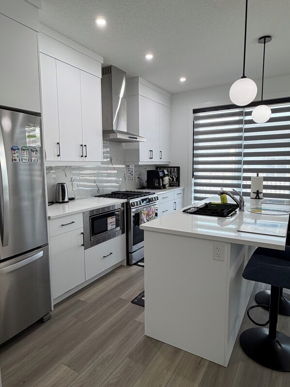 A modern kitchen with white cabinetry, stainless steel appliances, a central island, and a window with blinds.