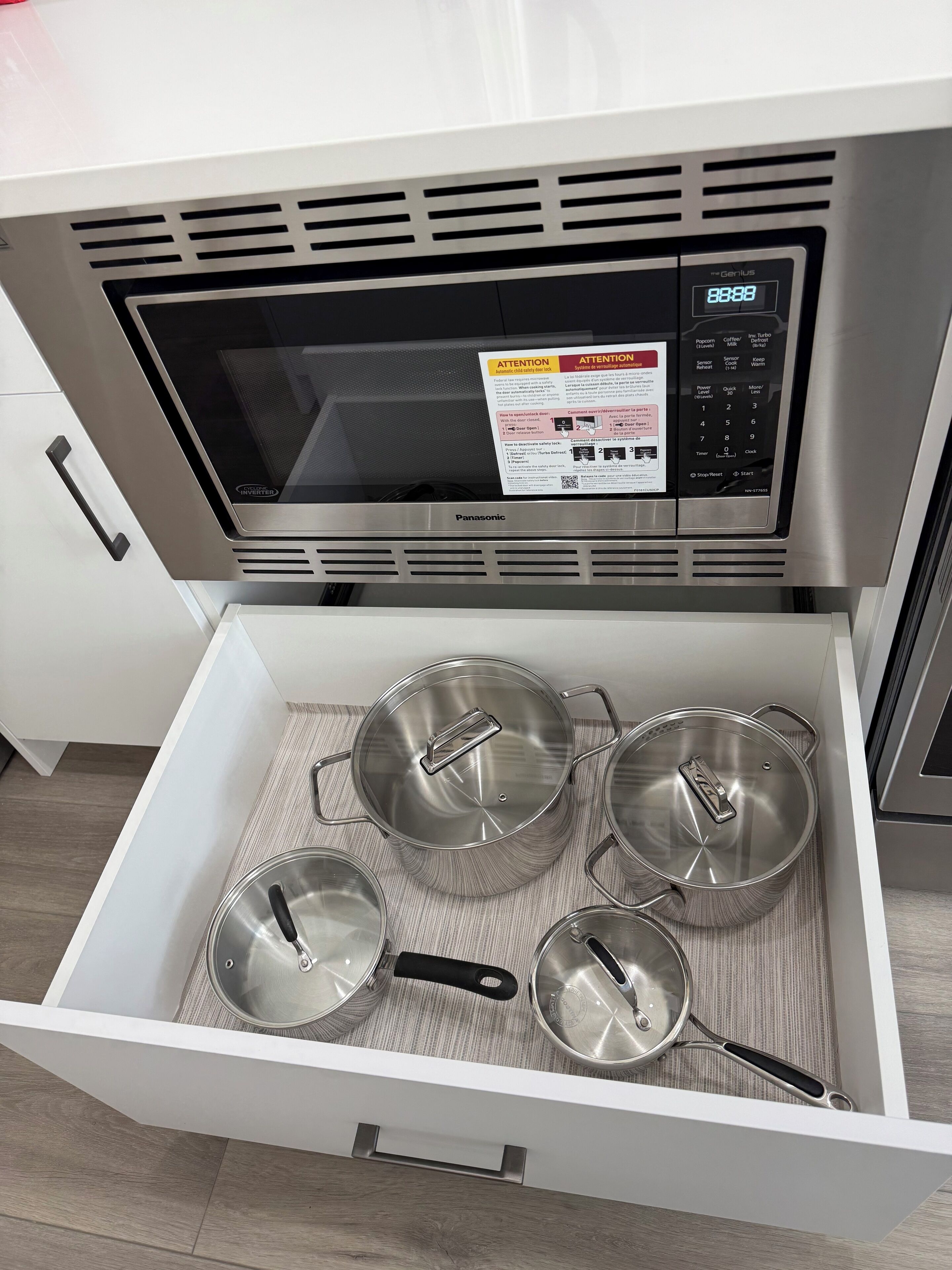 Uma gaveta de cozinha com um micro-ondas e quatro panelas de aço inoxidável.
