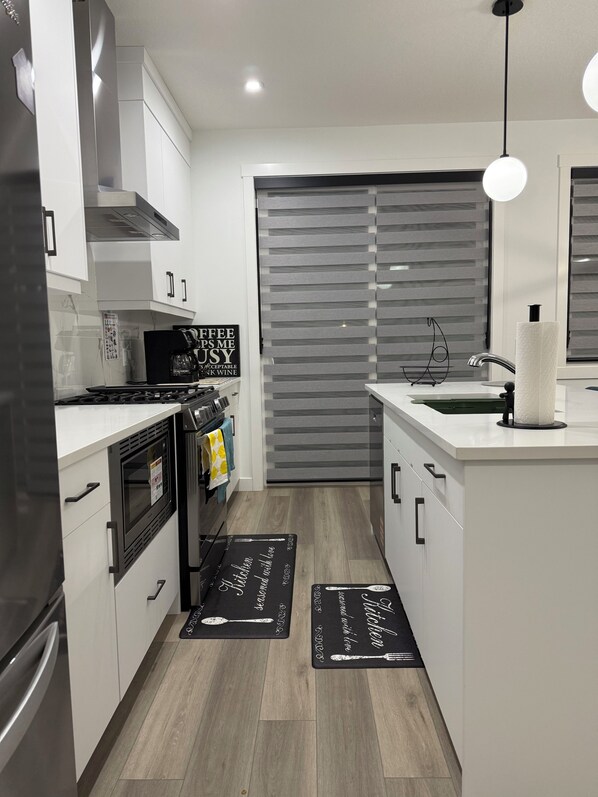 A modern kitchen with white cabinets, a black stove, a microwave, and a sink. There are black mats on the floor with kitchen-themed designs.