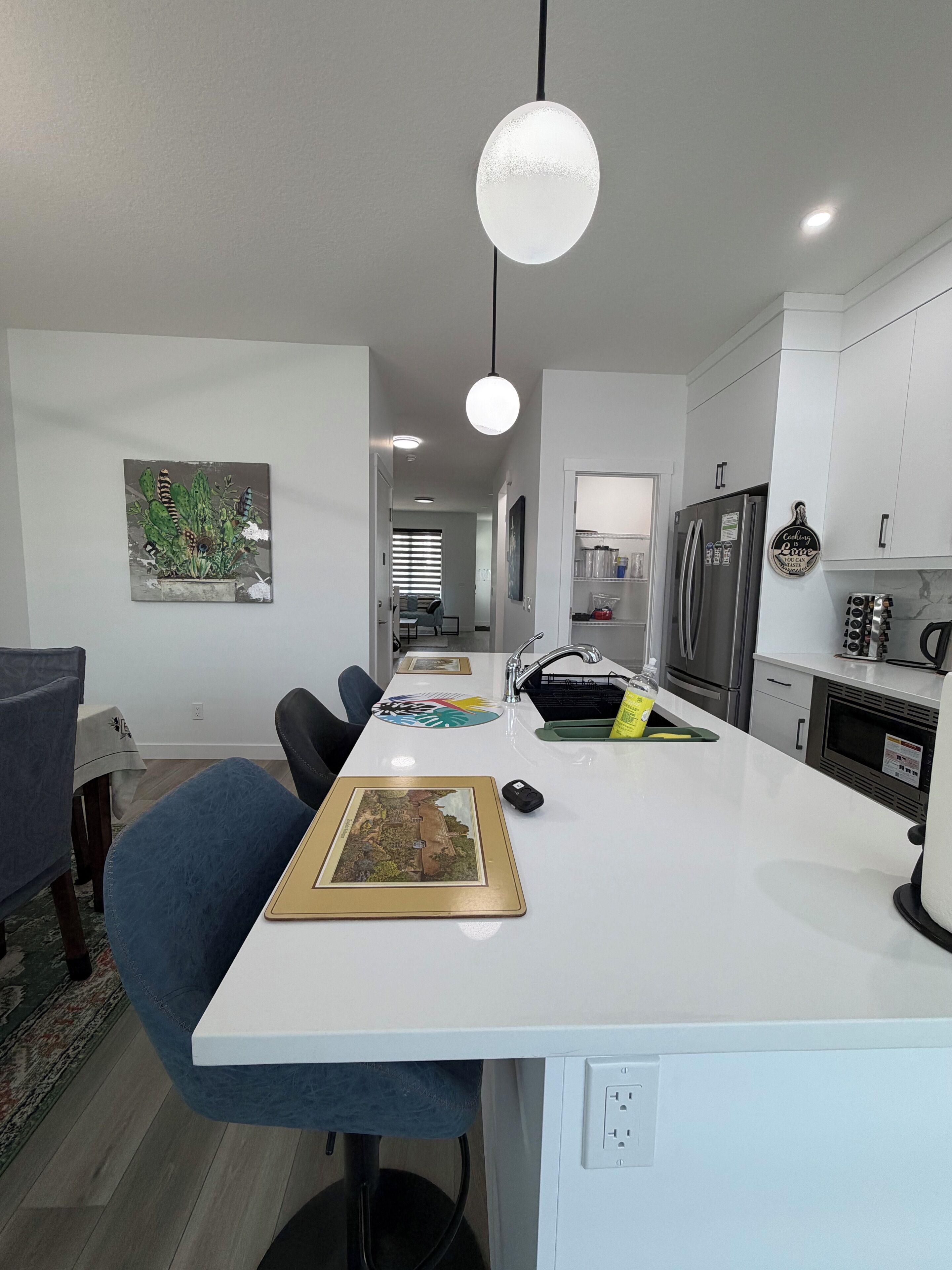 Una cucina moderna con mobili bianchi, un'isola centrale e un'area pranzo con una sedia blu.